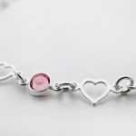 a silver bracelet with three hearts and a pink stone
